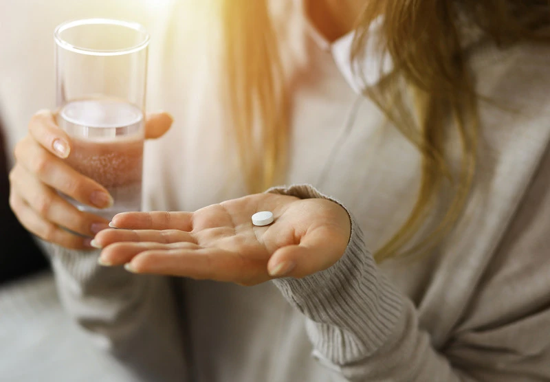 A woman holding a pill and a water glass
