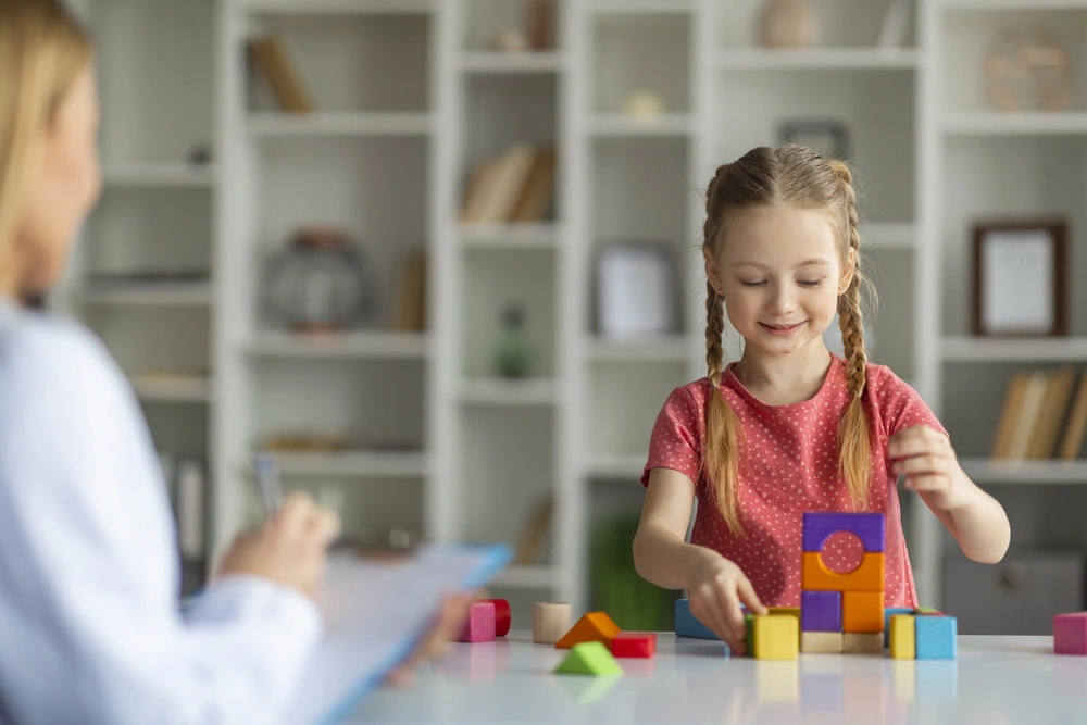 little girl making pyramids from wood blocks during meeting with psychotherapist