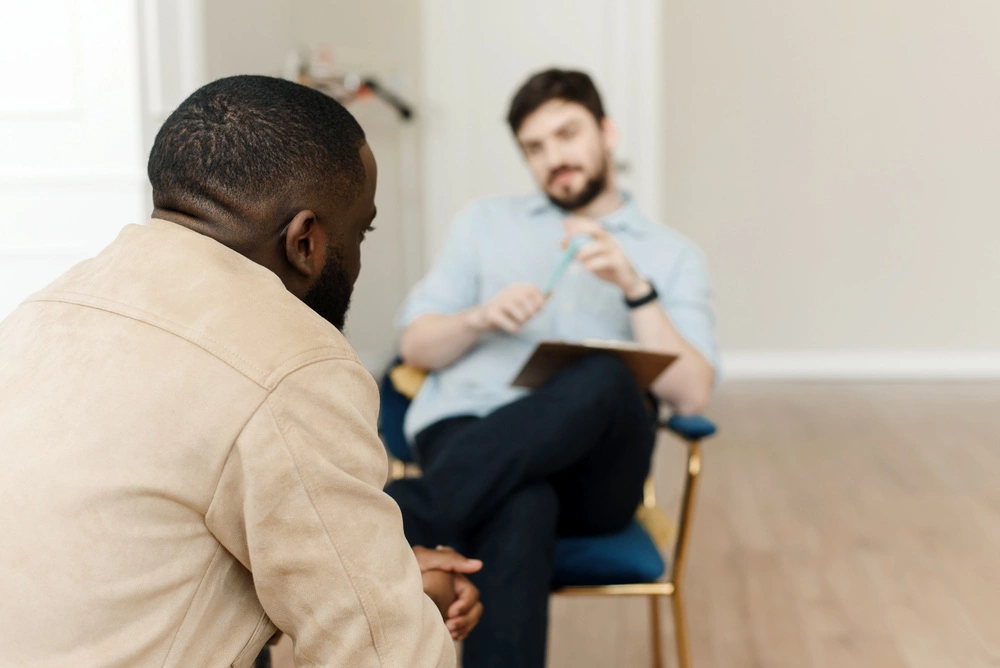 unhappy young black man having session with professional psychologist at mental health clinic