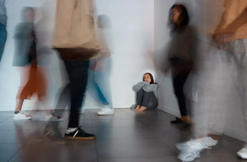 Person sitting on the floor, overwhelmed by a panic attack, while others walk by.