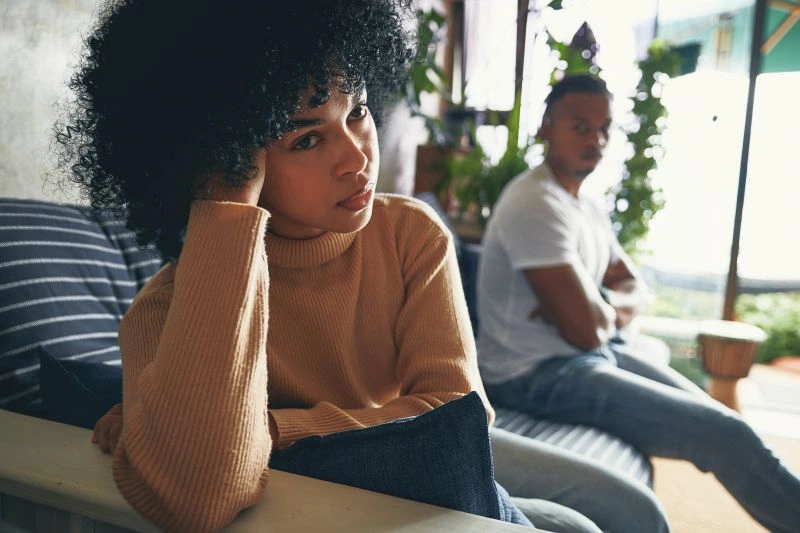 A woman sitting on a couch, looking upset while a man sits beside her, showing signs of relationship tension. Therapists for relationship anxiety help couples manage emotional distress and improve communication.
