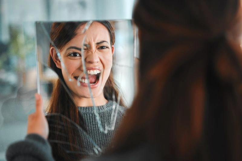 A woman looking into a broken mirror, expressing emotional pain. This image may reflect the emotional struggles and challenges of self-image often experienced by individuals with Borderline Personality Disorder (BPD), which can impact their capacity for stable love.