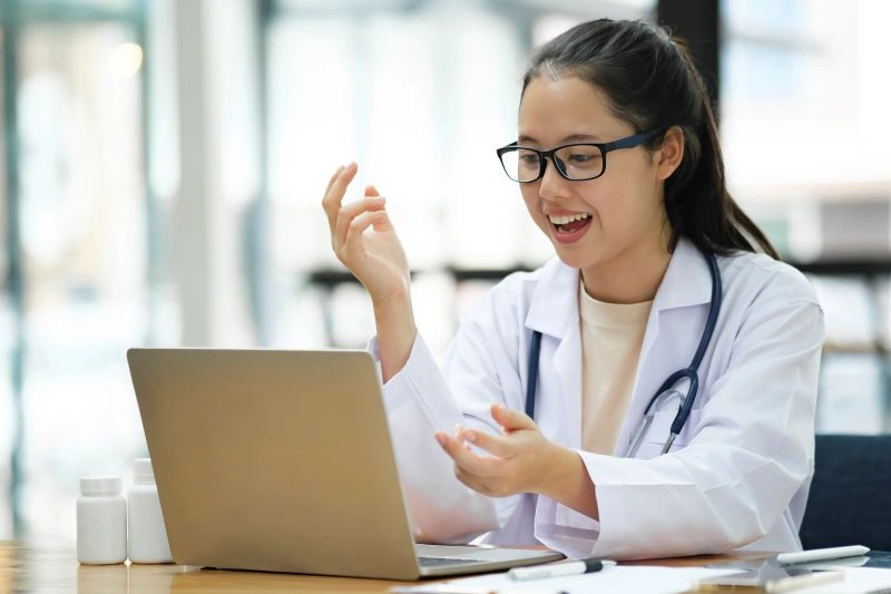 A female psychiatrist in a white coat engaging with a patient via video call on her laptop. Online psychiatrist prescriptions allow for remote consultations and medication management for mental health conditions.
