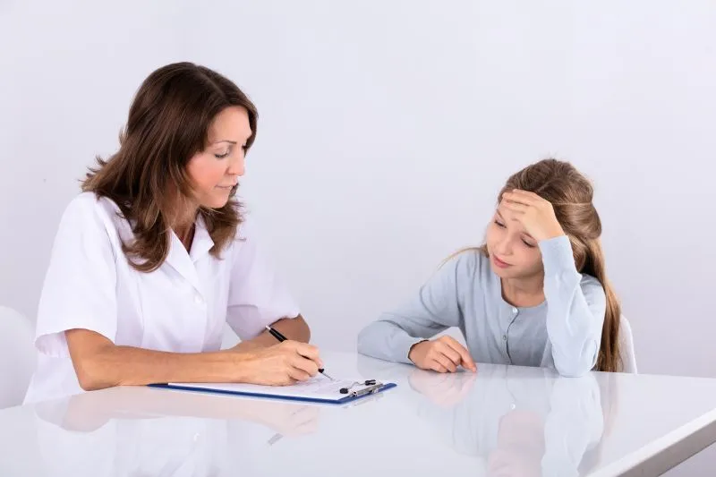 A healthcare professional conducting an ADHD assessment for a child. The doctor is taking notes while the child, who appears thoughtful or anxious, sits at a desk, engaging in the assessment process.