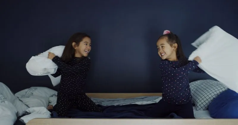 Two young girls enjoying a playful pillow fight on a bed. This joyful moment captures the carefree side of childhood, which contrasts with the focus of ADHD assessment for child, emphasizing the importance of understanding both playful and behavioral aspects of a child's development