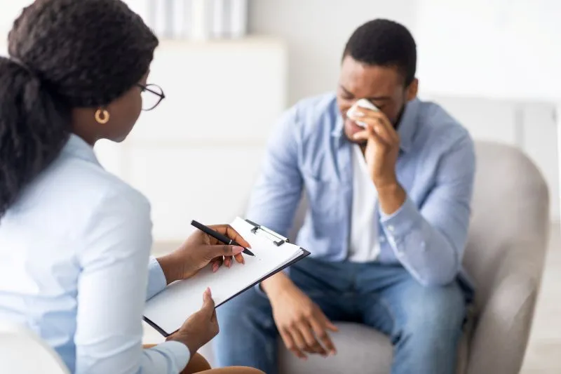 A therapist taking notes during a session with a patient visibly distressed and wiping tears, demonstrating the emotional challenges of mood disorders and treatment. This scene emphasizes the importance of therapy in managing mood-related issues.