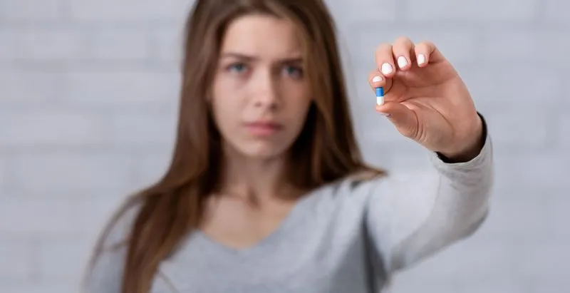 A woman holding a blue pill, representing the action of taking mental health medications. This image emphasizes the importance of knowing who can prescribe mental health medications, highlighting the professionals involved in the process.