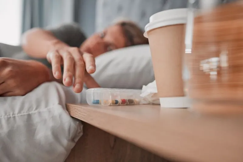 A person reaching for a pillbox filled with various medications on their bedside table, indicating the importance of finding the best ADHD medication for adults with anxiety to manage both conditions effectively.