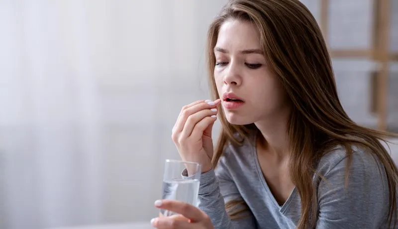 Young woman holding a glass of water and preparing to take a pill, symbolizing the signs your antidepressant dose is too low.